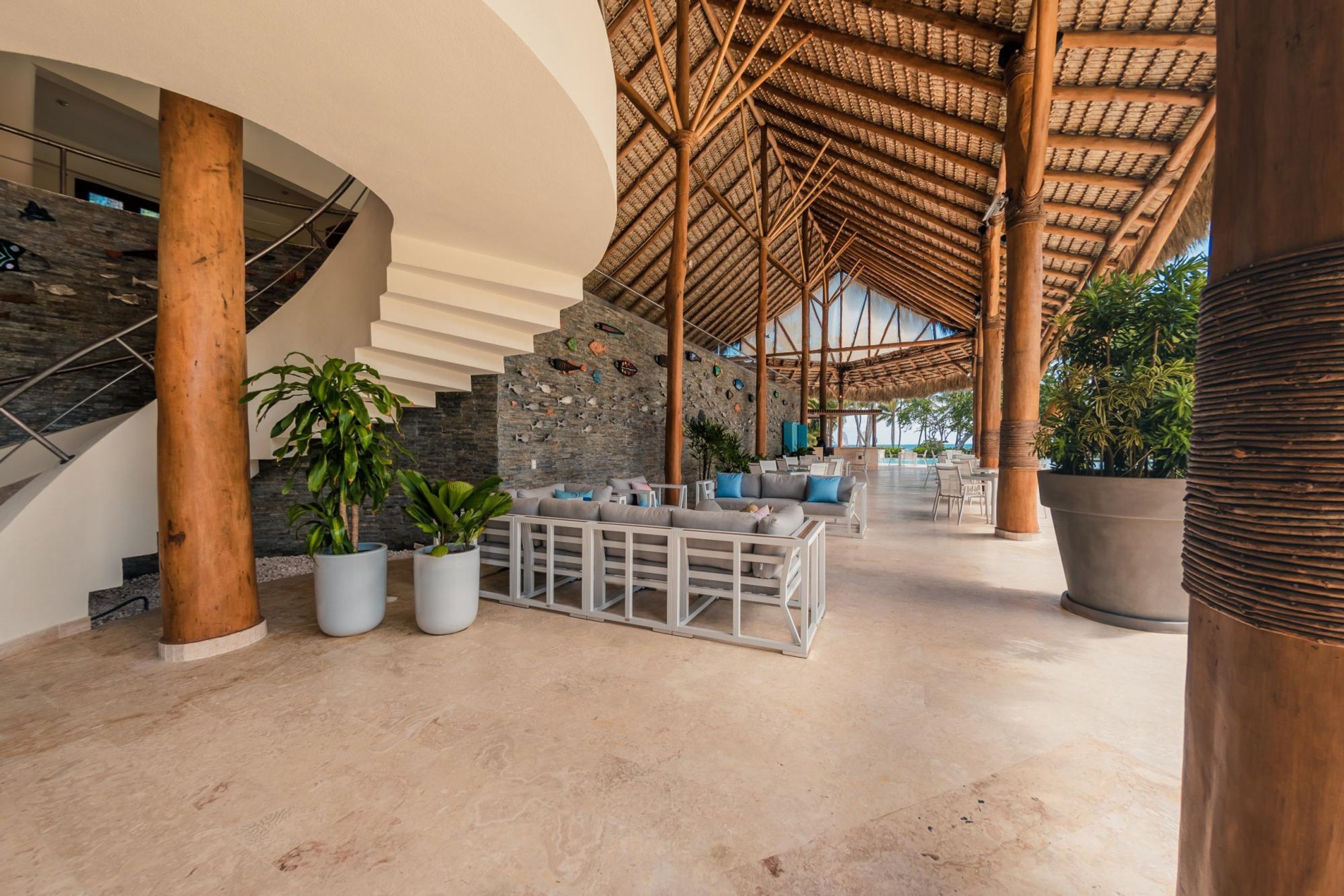 A spacious lobby with a curved staircase, a large seating area, and a thatched roof structure.