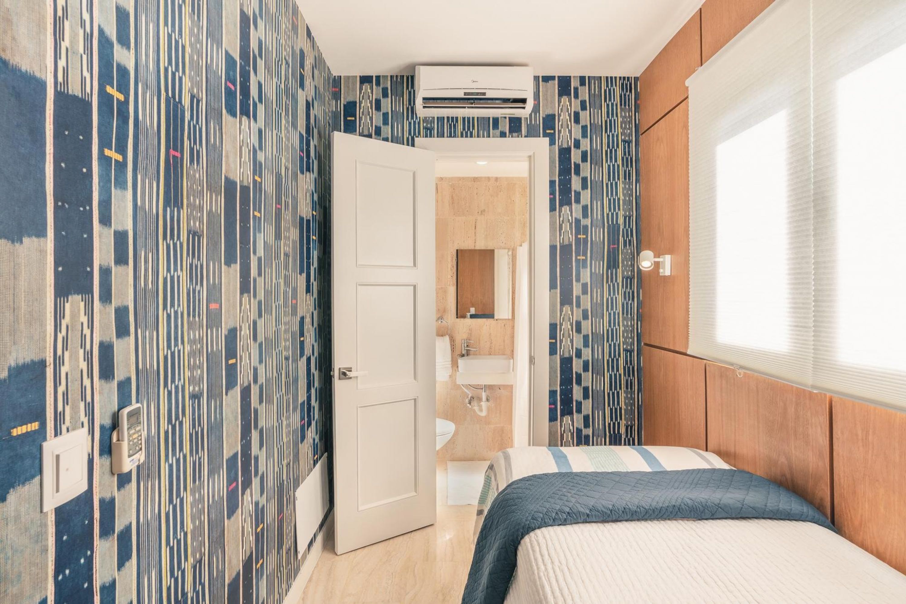 A bedroom with a bed, a bathroom with a toilet and sink, and a patterned wall.