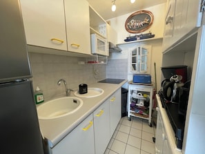 A compact kitchen with white cabinets, a double sink, a coffee machine, and a small refrigerator.