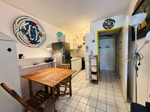 Eine kleine Küche mit Essecke, einem Kühlschrank, einer Spüle und einem Wandbild.