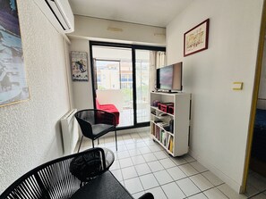 Una habitación con una silla negra, un mueble blanco para televisor con una pantalla plana, una estantería y un sofá rojo.