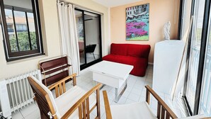 Een kamer met een witte tafel, houten stoelen, een rode bank, een radiator, een raam en een schilderij aan de muur.