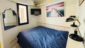 Een slaapkamer met een bed, een televisie, een schilderij, een spiegel en een bureaulamp.