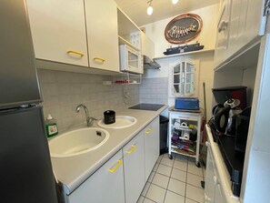A compact kitchen with white cabinets, a double sink, a coffee machine, and a small refrigerator.