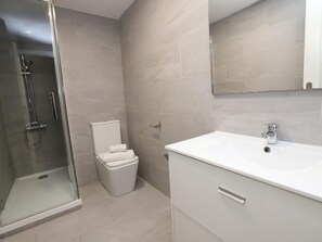 Une salle de bain moderne avec une douche à parois de verre, des toilettes et un lavabo blanc avec un miroir au-dessus.