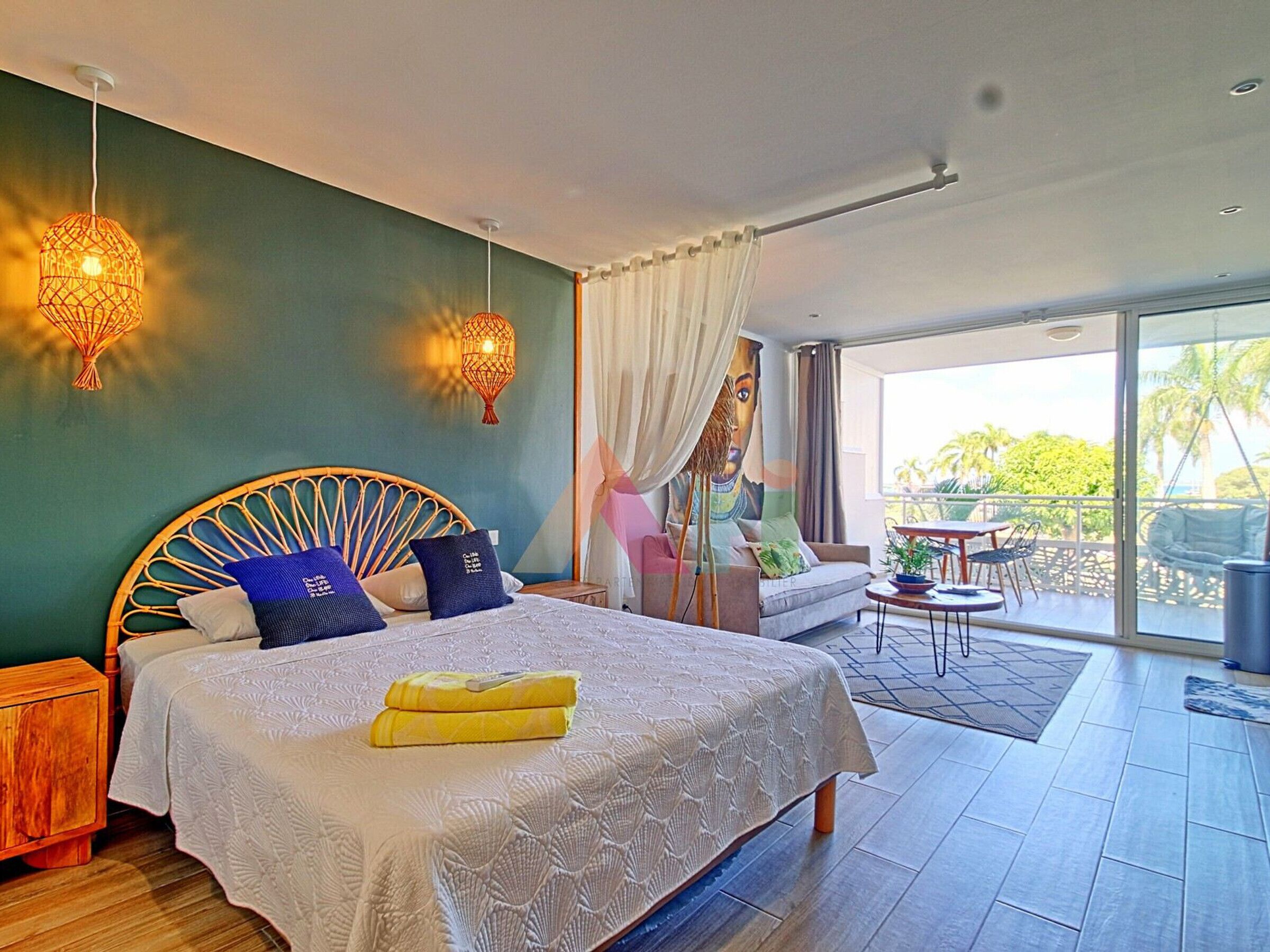 Ein Schlafzimmer mit einem großen Bett, zwei Wandlampen, einer Couch und einem Balkon mit Tisch und Stühlen.