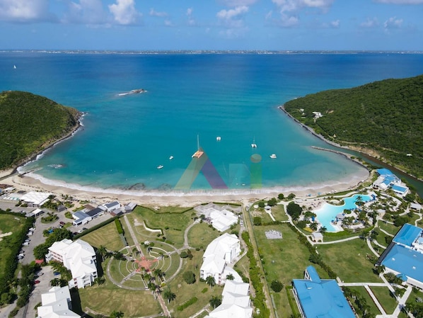 An aerial view of a coastal resort with a beach, swimming pool, and several buildings.