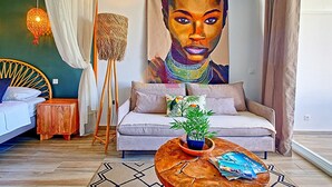 A modern living room with a sofa, a coffee table with magazines, a floor lamp, a painting on the wall, and a bed with a headboard. - Studio in Anse Marcel, beach, air conditioning, parking (Saint-Martin)