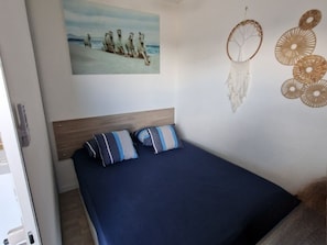 A bedroom with a bed, a wall-mounted dreamcatcher, and a painting. - Charming 2-Room Apartment with Pool, Terrace, and A/C - 4 Sleeps - Near Port and Beach (Port Camargue)