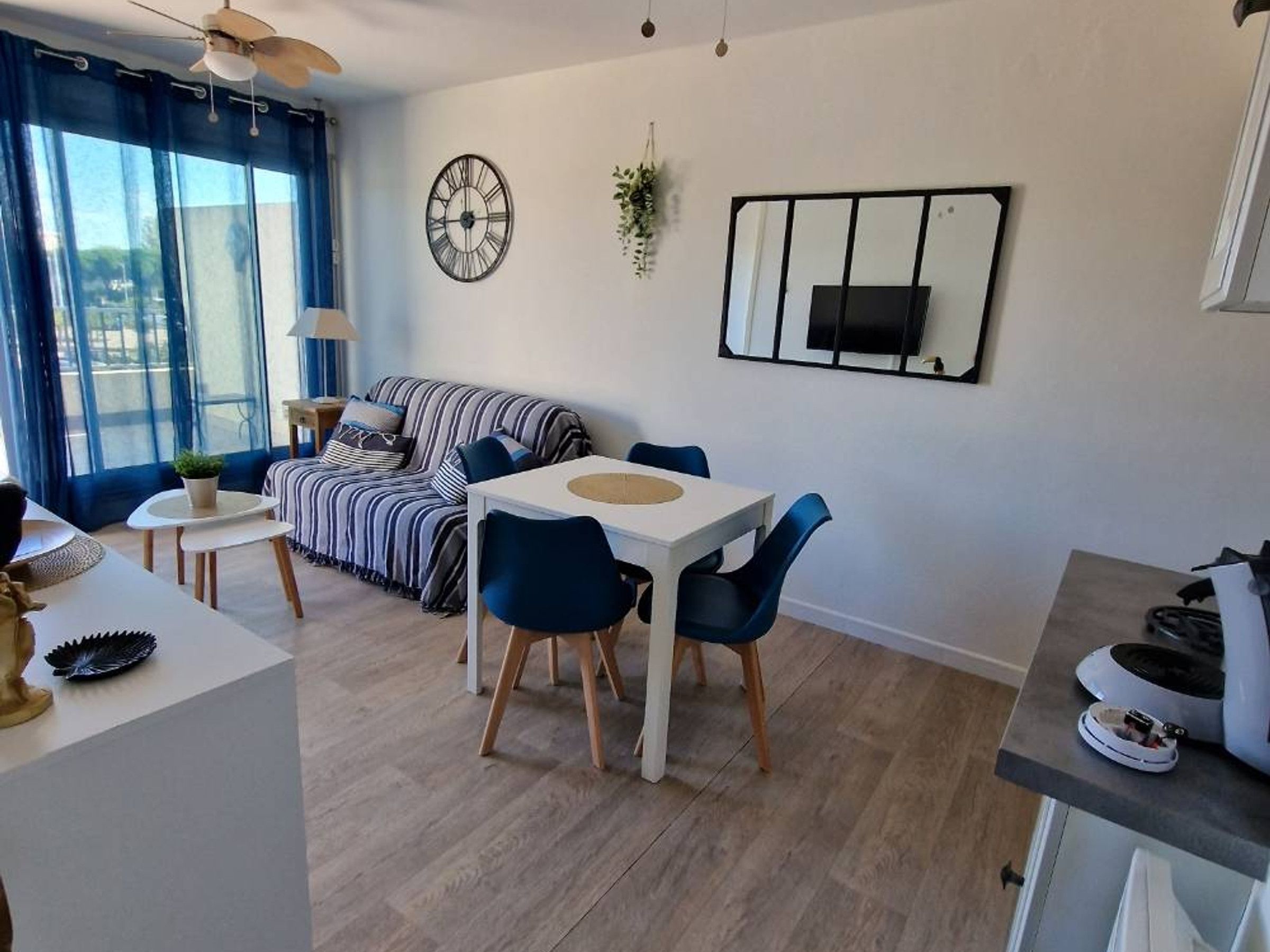 Ein modernes Wohnzimmer mit einer Couch, einem Esstisch mit Stühlen, einer Uhr und einem Fernseher an der Wand.