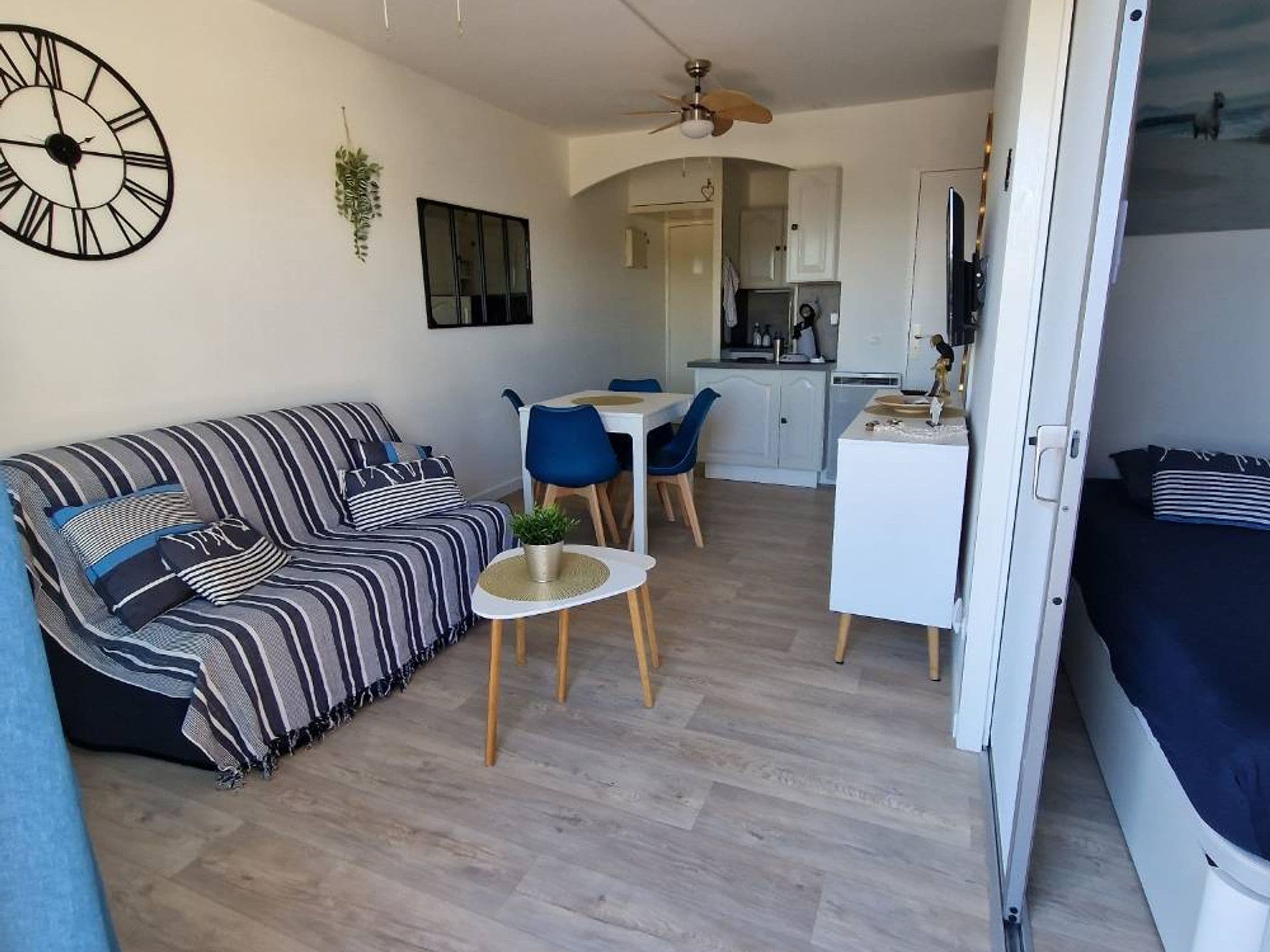 A compact living space with a sofa, a small dining table, a kitchenette, and a ceiling fan.