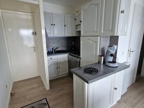 A compact kitchen with white cabinetry, a built-in stove, and a coffee machine. - Charming 2-Room Apartment with Pool, Terrace, and A/C - 4 Sleeps - Near Port and Beach (Port Camargue)