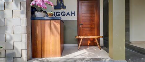 A wooden counter with a vase of pink flowers, a door, and a small bench.