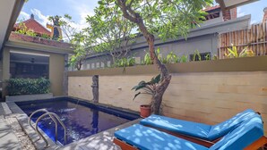 Una piscina con escalera metálica, rodeada por un muelle de madera y una valla de bambú.