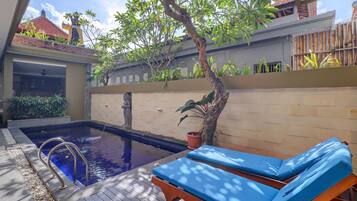 A swimming pool with a metal ladder, surrounded by a wooden deck and a bamboo fence.