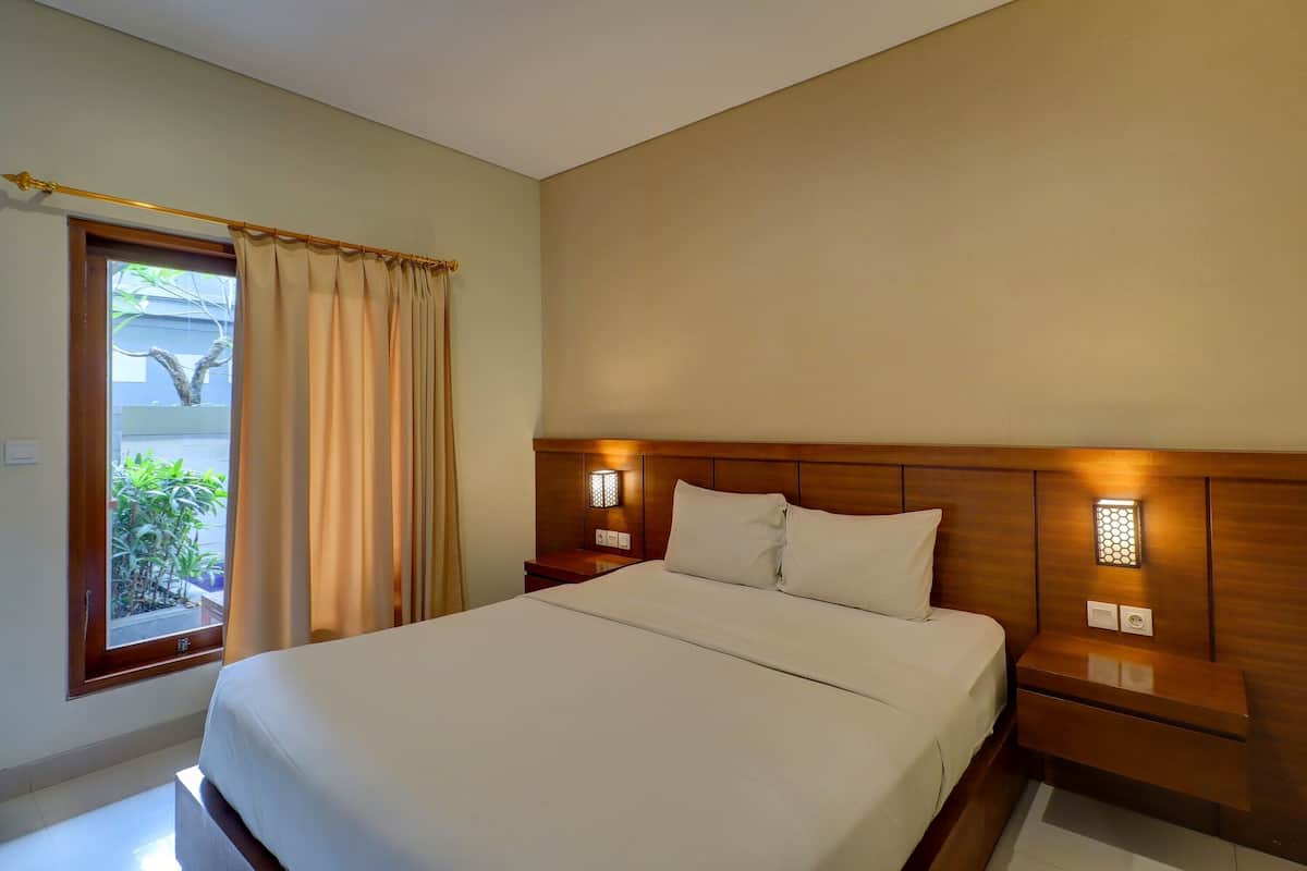 Habitación de hotel con una cama grande, cabecero de madera, lámparas de noche y una ventana con cortinas.