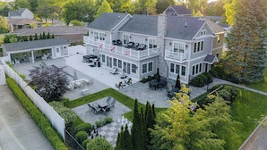 A two-story house with a covered patio, outdoor seating, and a well-maintained lawn. - Resort Pool Home | Walk to Beach | 7 BR | Dogs (South Haven)