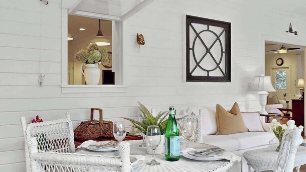 A dining area with white wicker furniture, a table set for two, and a bottle of wine. - Resort Pool Home | Walk to Beach | 7 BR | Dogs (South Haven)