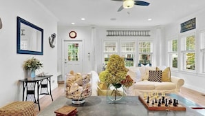 A spacious living room with a large window, a sofa, a coffee table, and a chessboard. - Resort Pool Home | Walk to Beach | 7 BR | Dogs (South Haven)