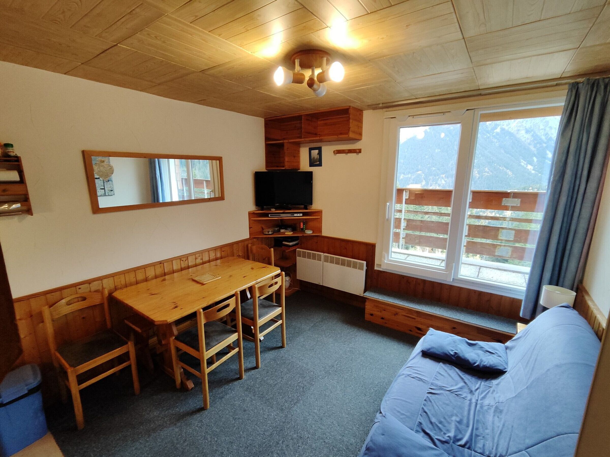 L’intérieur d’un chalet accueillant, avec une table à manger en bois, des chaises, un canapé, un téléviseur et une fenêtre donnant sur les montagnes.