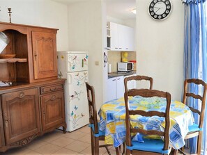 A compact kitchen with wooden cabinets, a white refrigerator with colorful bird decals, a microwave, and a dining area with a table covered in a blue and yellow tablecloth.