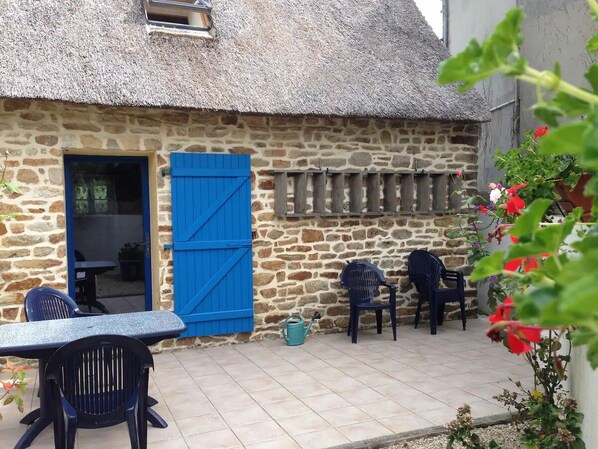 A stone building with a thatched roof, a blue door, and a small outdoor seating area with chairs and a table. - Chaumière Typiquement Bretonne (Concarneau)