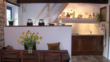 Une cuisine rustique avec des meubles en bois, un pare-feu en carreaux et un petit îlot central agrémenté d’un vase de fleurs jaunes.