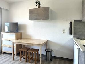 Uma cozinha compacta com mesa de madeira, banquetas, lixeira e televisão em um armário.