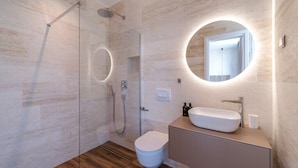 Een moderne badkamer met een douchecabine van glas, een ronde spiegel en een wit wastafel.