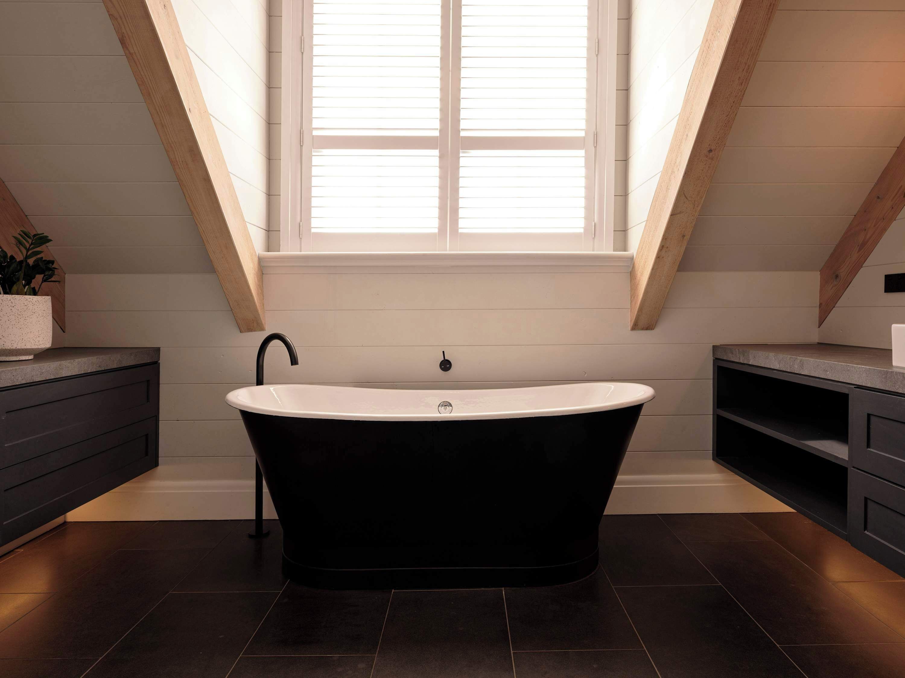 Une salle de bain moderne avec une baignoire sur pieds, des poutres en bois et une fenêtre.