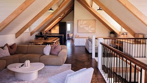 Een kamer in loftstijl met zichtbare houten balken, een bank, een eettafel en een trap.