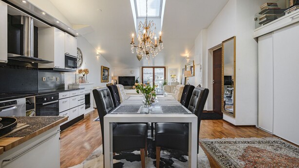 A modern kitchen with a dining area, featuring a chandelier, a large window, and a view of the city. - Luxus penthouse in great location (Helsinki)