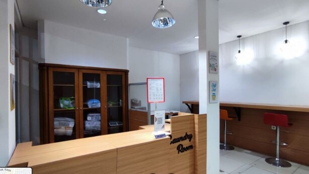 A hotel reception area with a wooden counter, a sign indicating a laundry room, and a bar area with stools. - OYO Life 92779 Kost Arjuna (Tangerang)