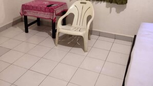 A small room with a tiled floor, a white plastic chair, a small table with a pink tablecloth, a mirror on the wall, and a green curtain. - OYO Life 92779 Kost Arjuna (Tangerang)