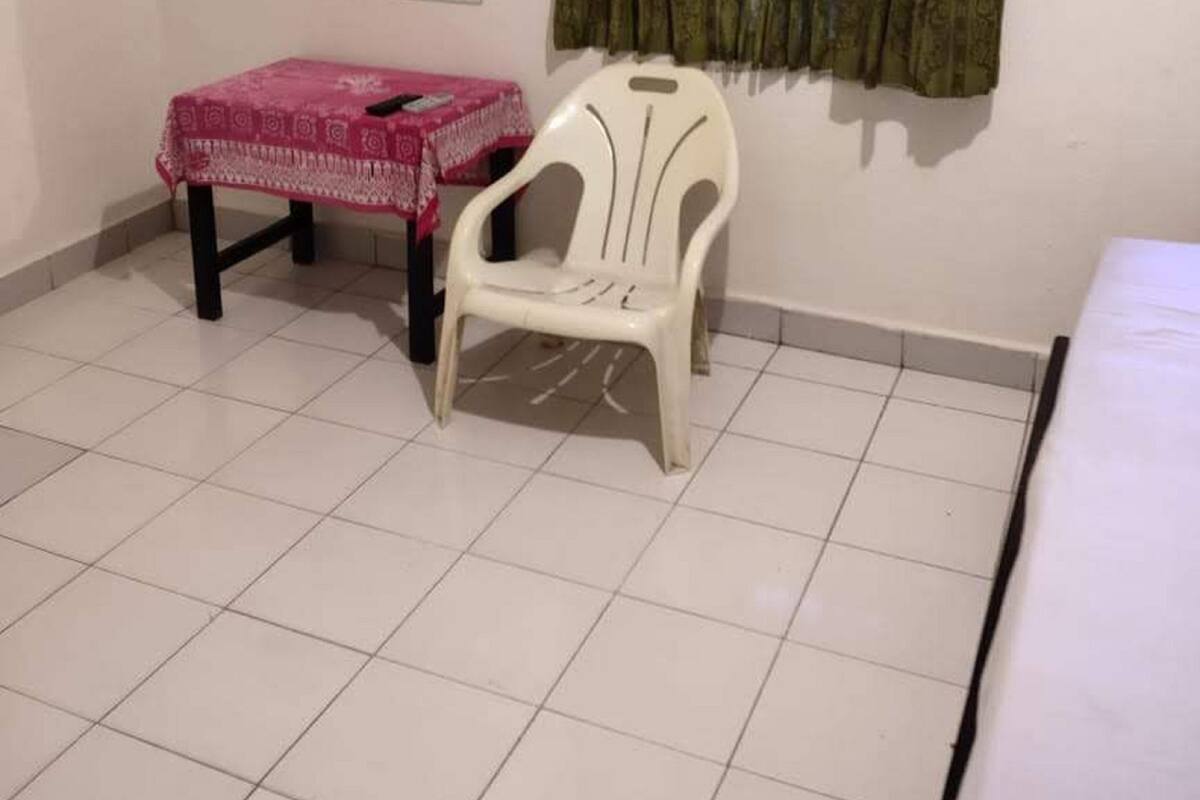 Una habitación pequeña con piso de baldosas, una silla de plástico blanca, una mesa con mantel rosa, un espejo en la pared y una cortina verde.