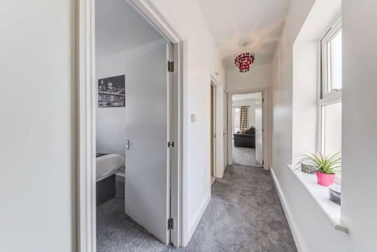 A hallway with a white door leading to a bathroom, a window with a plant, and a ceiling light fixture.