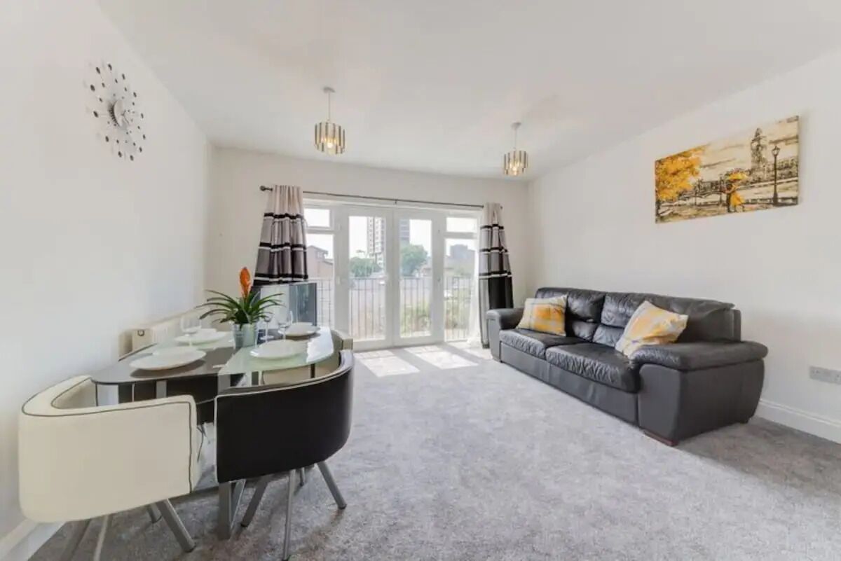 A modern living room with a dining area, a grey sofa, and a painting on the wall.