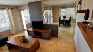 A modern living room with a flat-screen TV, wooden coffee table, and a dining area with a table and chairs. - Palmzicht (Cape Town)