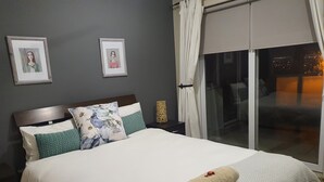 A neatly made bed with a rolled towel, two framed pictures on the wall, and a view of the city at night through the window. - Palmzicht (Cape Town)