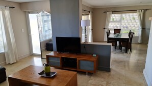 A spacious living room with a flat-screen TV, a wooden coffee table, and a dining area with a table and chairs. - Palmzicht (Cape Town)