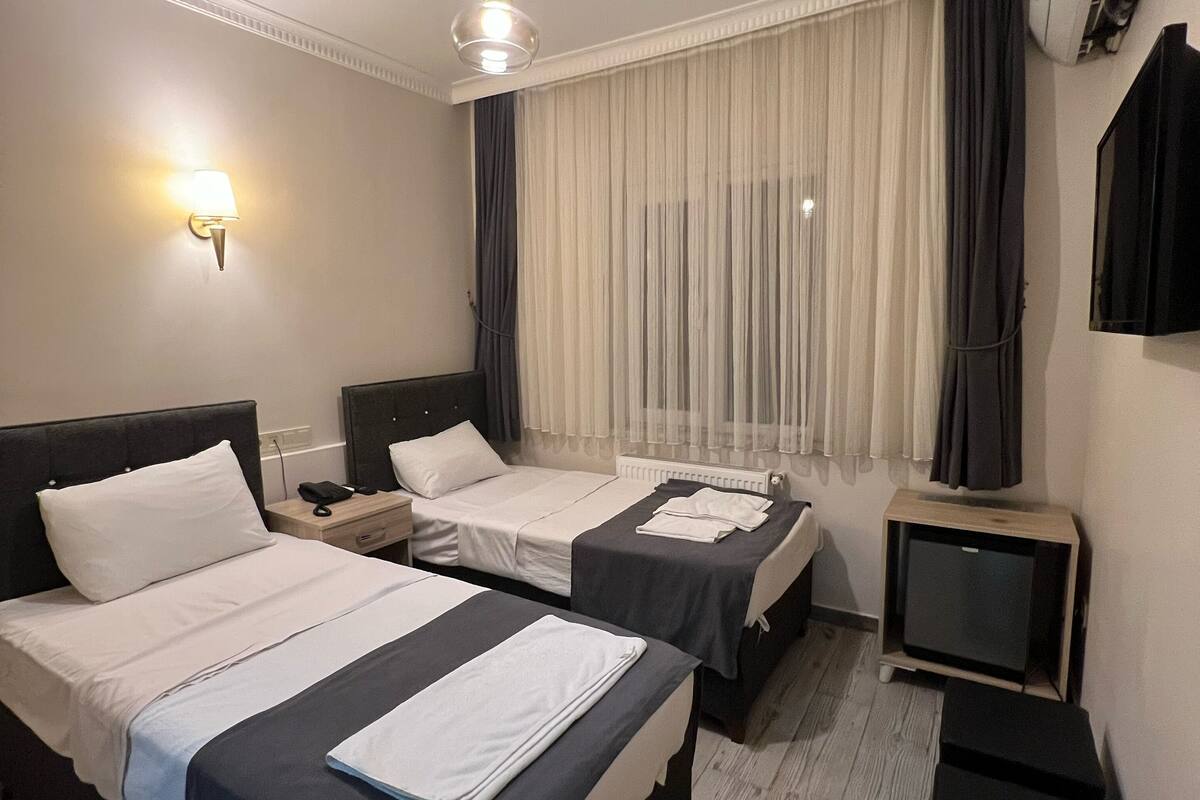 Quarto de hotel com duas camas, um ventilador de teto, televisão e ar condicionado fixado na parede.