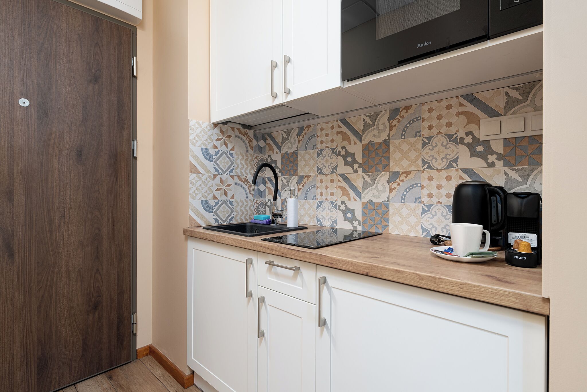 Et kompakt køkken med træbordplade, hvide skabe og et mønstret backsplash.