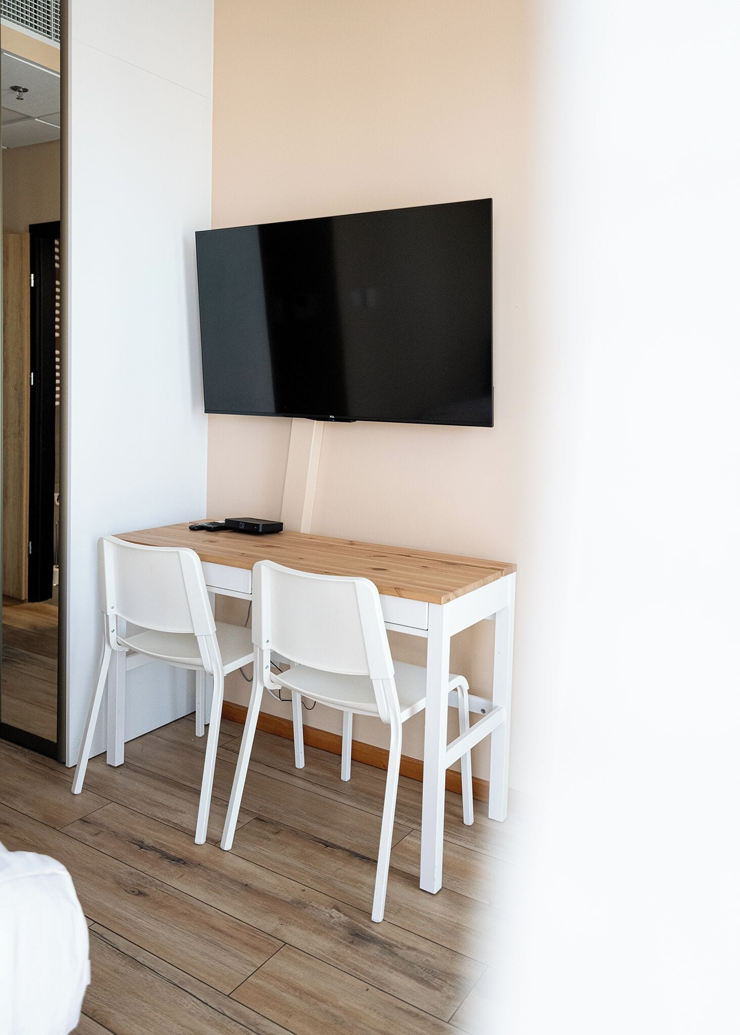 A modern room with a wooden desk, two white chairs, and a flat-screen TV mounted on the wall.