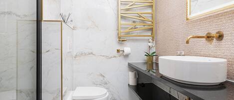 Un baño moderno con cabina de ducha de vidrio, inodoro blanco, espejo con marco dorado y tocador negro con lavabo blanco.
