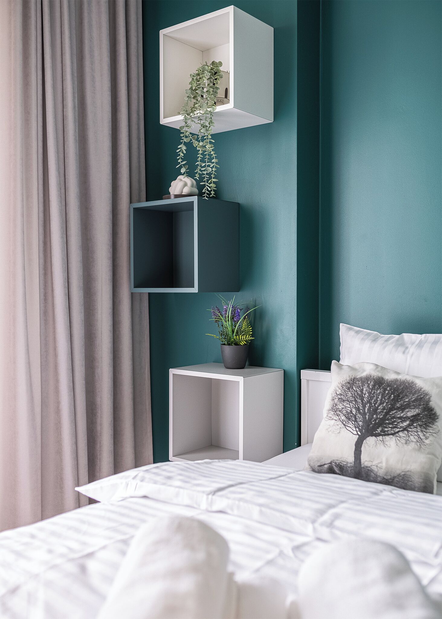 Un dormitorio con paredes verde azulado, una cama blanca, una cortina gris y una mesita de noche blanca con una planta en maceta.