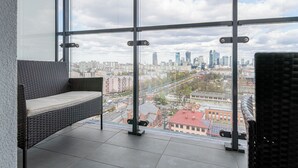 A balcony with a wicker sofa and a view of a cityscape through large windows. - RentPlanet - Studio Kasprzaka (Warsaw)