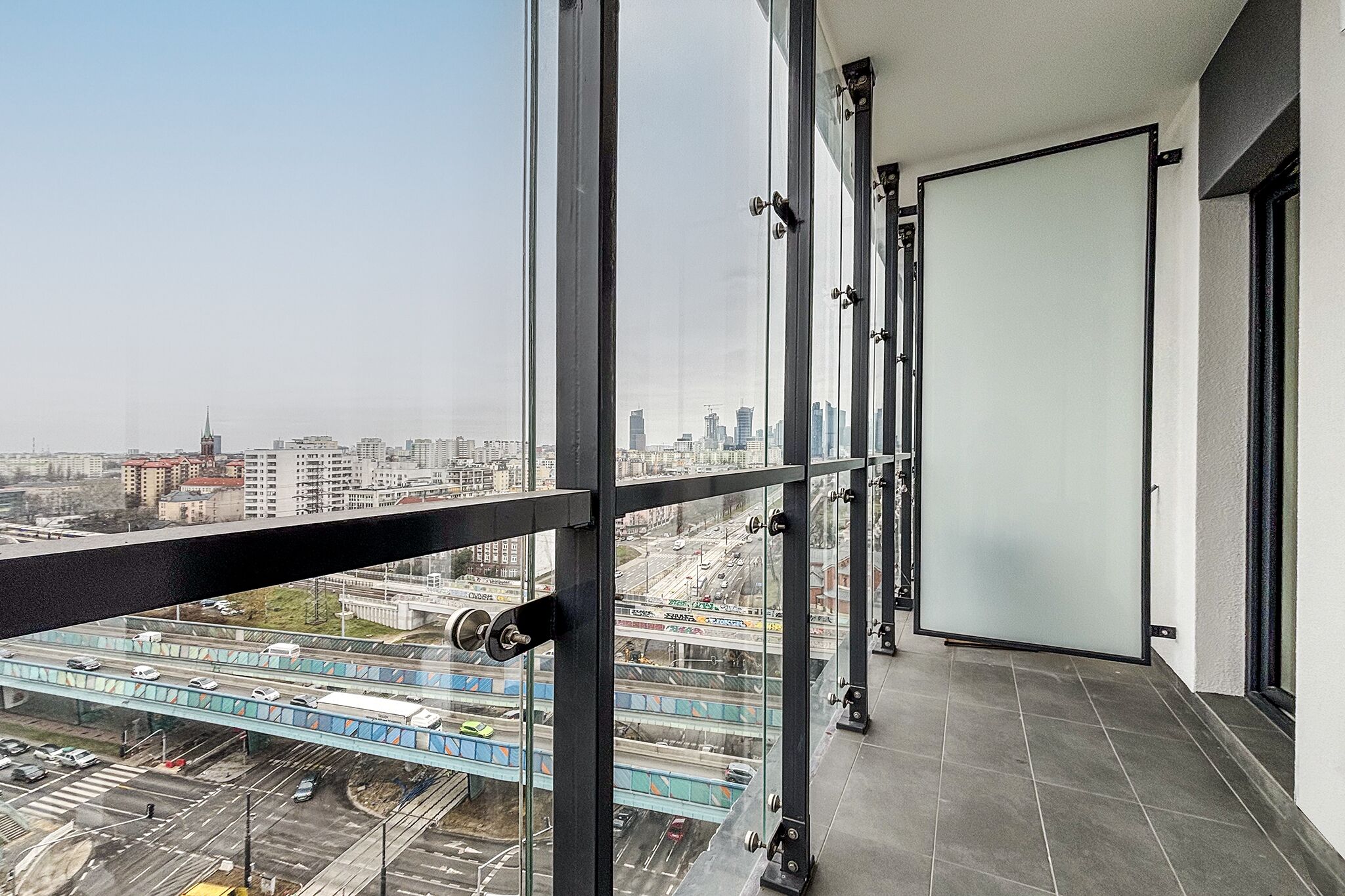 Un balcon situé dans un immeuble de grande hauteur, offrant une vue sur la ville, notamment sur un pont et des bâtiments.