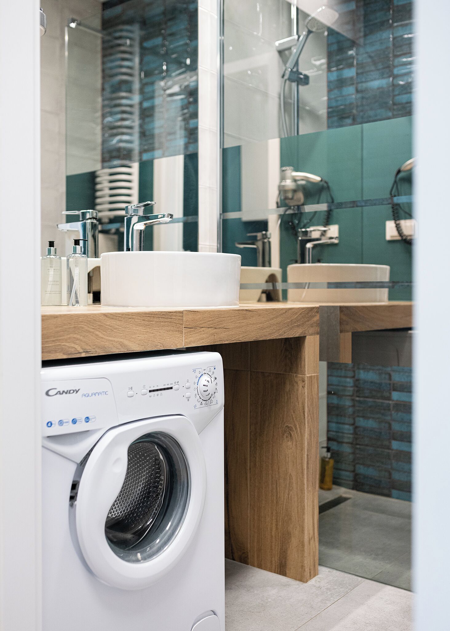 A modern bathroom with a large mirror, a sink, and a Candy Aquatronic washing machine.