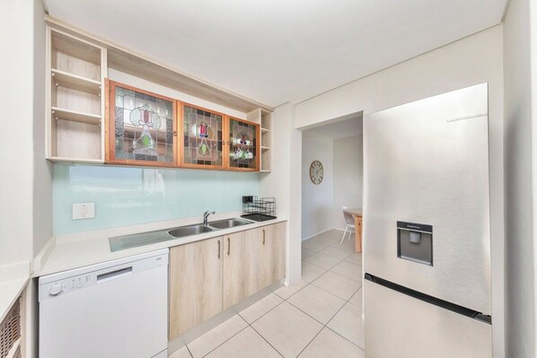 A modern kitchen with a dishwasher, a stainless steel refrigerator, and a built-in cabinet with glass doors.