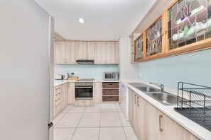 Une cuisine compacte avec des meubles de couleur bois clair, un four à micro-ondes, une cuisinière et un évier.
